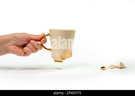 Ein Mann, der eine zerbrochene Teetasse isoliert auf weißem Hintergrund hält. Nahaufnahme des Arms mit gerissener Kaffeetasse Stockfoto