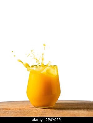 Ein Glas frischer Orangensaft auf einem Holztisch mit weißem Hintergrund. Dynamisches Gießen von Fruchtsaft am Morgen. Stockfoto