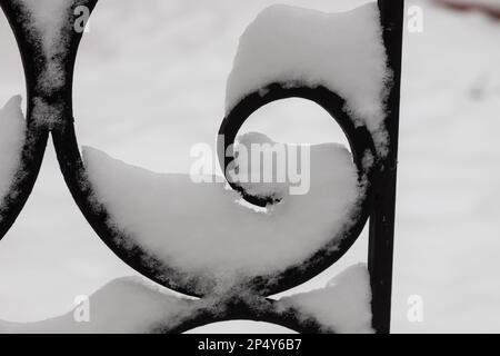 Bruchstücke eines schmiedemetallenen schwarzen Zauns, der nach Schneefall mit Schnee bedeckt ist. Stockfoto