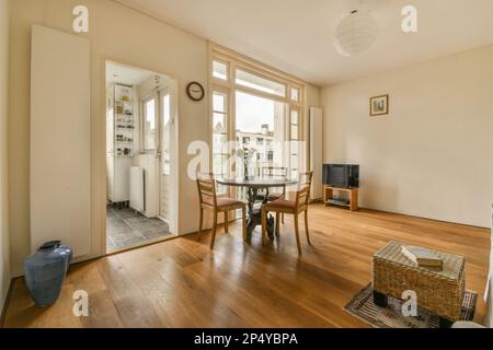 Amsterdam, Niederlande - 10. April 2021: Ein Wohnzimmer mit Holzfußboden und weißen Wänden, einschließlich eines runden Esstisches umgeben von Korbweiden Stockfoto