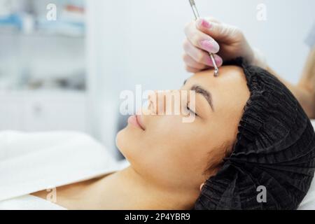 Schönheitsspritzen. Kosmetologe stellt verjüngende Anti-Falten-Injektionen an der Stirn einer Weißen her. Kosmetik der Frau im Schönheitssalon. Hübsch Stockfoto