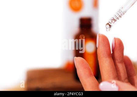 Extreme Nahaufnahme von Frauenhand und Pipette. Transplantattropfen Essenz, Öl oder Gel tropfen aus der Pipette. Verschwommene braune Glasflasche auf dem B Stockfoto