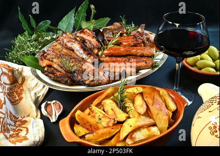Gemischter Fleischgrill im Romagnola-Stil mit Würstchen, Schweinebauch, Lebern mit Netzen, Schweinerippchen, Koteletts und gebackenen Kartoffeln mit Knoblauch und Rosmarin Stockfoto