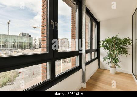 Amsterdam, Niederlande - 10. April 2021: Ein Raum mit großen Fenstern und einer Pflanze in der Ecke auf der rechten Seite des Fotos ist ein Bürogebäude Stockfoto