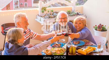 Mittagspause im Alter. Eine Gruppe von Rentnern, die draußen am Tisch essen und trinken, anstoßen und Feiertage feiern. - Alles Gute Stockfoto