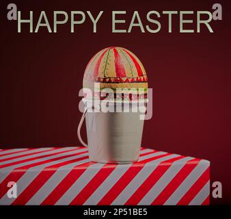 Handbemaltetes Osterei in einem weißen Eierbecher auf einer gestreiften Oberfläche mit rotem abgestuftem Hintergrund. Stockfoto