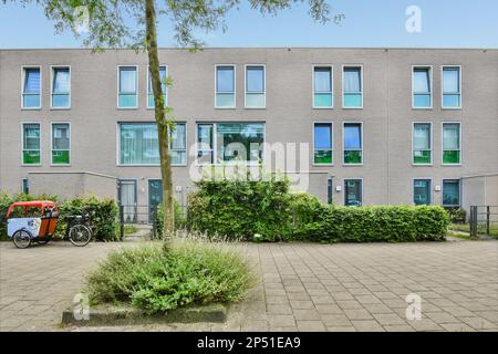 Amsterdam, Niederlande - 10. April 2021: Ein Fahrrad vor einem Gebäude mit vielen Fenstern und Pflanzen, die auf dem Boden neben dem Bürgersteig wachsen Stockfoto