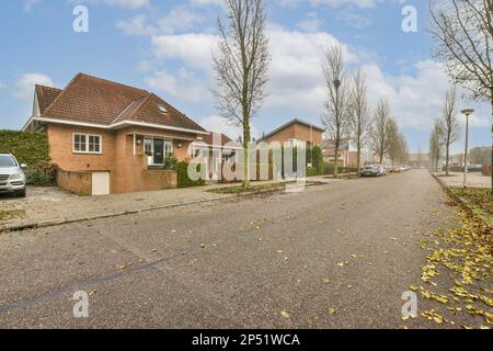 Eine leere Straße mit Blättern auf dem Boden und Häuser im Hintergrund unter einem blauen Himmel gefüllt mit weißen Wolken Stockfoto