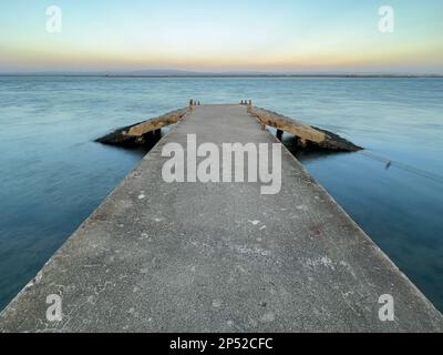 Leerer Betonpier zur Ria de Aveiro in Portugal mit dramatischem Himmel und ruhigem Wasser. Stockfoto