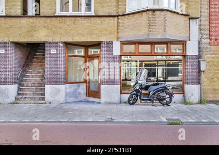 Amsterdam, Niederlande - 10. April 2021: Ein Motorrad, das vor einem Gebäude geparkt ist, mit Treppen zur Tür und einem offenen Fenster auf der rechten Seite Stockfoto