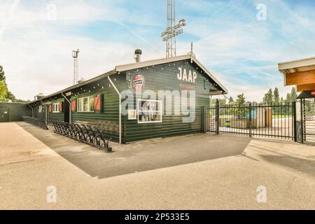 Amsterdam, Niederlande - 10. April 2021: Ein kleines grünes Gebäude mit einem Schild an der Seite und einem schwarzen Metallzaun um den Eingang des Gebäudes Stockfoto