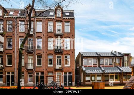 Amsterdam, Niederlande - 10. April 2021: Ein Apartmentkomplex mit Fahrrädern, die auf dem Bürgersteig vor ihm stehen, und mehreren Gebäuden auf der linken Seite Stockfoto