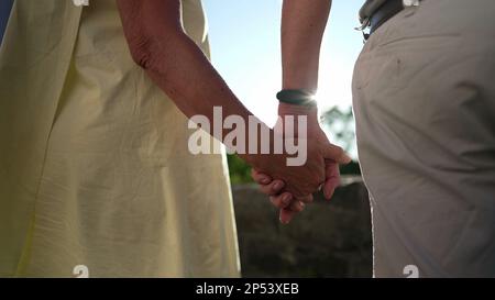 Das ältere Ehepaar hielt die Hände zusammen und stand draußen mit Sonnenschein. Nahaufnahme von verliebten und unterstützenden älteren Menschen Stockfoto