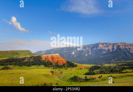 Grüne sanfte Hügel und große rote Felsen und Berge entlang des Chief Joseph Highway in einer sonnigen Sommerlandschaft in Wyoming Stockfoto