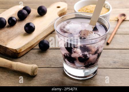 Brasilianischer jabuticaba Caipirinha in einem Glas mit Eis und Früchten auf einem Holztisch. Stockfoto