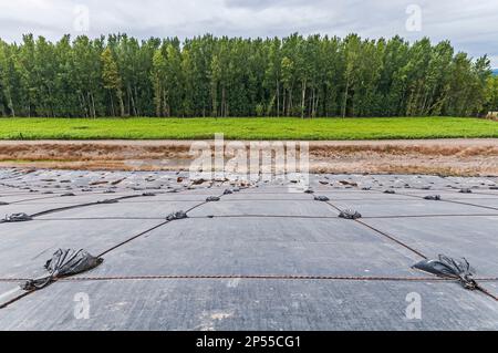 Beschichtete Kunststofffolien bedecken einen Hang in einer aktiven Deponie. Vermutlich PVC-Geomembranen mit einer Baumlinie in der Ferne. Stockfoto