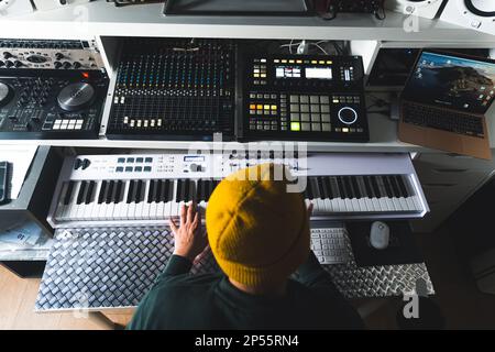 Junger Mann mit gelbem Hut, der in seinem Studio das elektrische Klavier spielt, Musikkonzept. Hochwertiges Foto Stockfoto