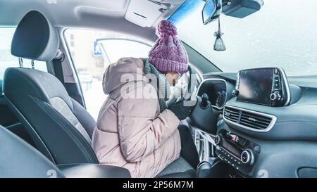 Mädchen sitzt in einem schneebedeckten Auto und wartet darauf, dass es anspringt. Hochwertiges Foto Stockfoto