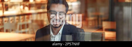 Ein lächelnder indischer Geschäftsmann im Anzug telefoniert während der Mittagspause im Café. Unscharfer Hintergrund Stockfoto