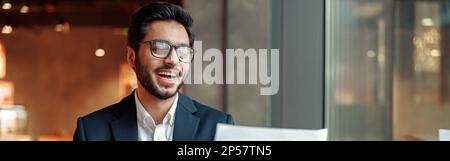 Lächelnder indischer Geschäftsmann, der Kaffee trinkt und im Café mit Dokumenten arbeitet Stockfoto