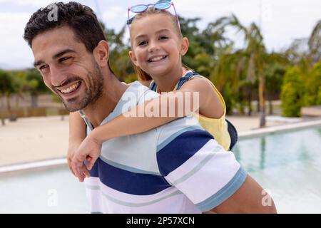 Porträt von glücklichen, birassischen Vater und Tochter, die sich am Swimmingpool umarmen Stockfoto