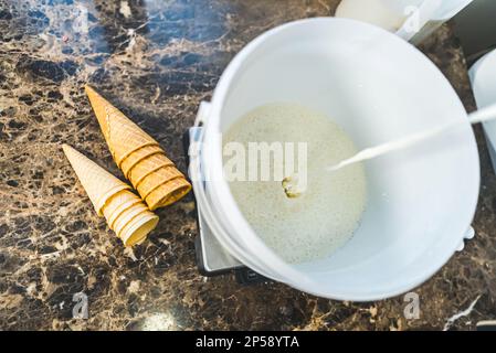 Eiscreme machen. Flüssige Vanille- oder Milcheis in einen weißen Eimer gegossen. Großer Blickwinkel. Leckere Eiskrem-Zwiebeln. Hochwertiges Foto Stockfoto