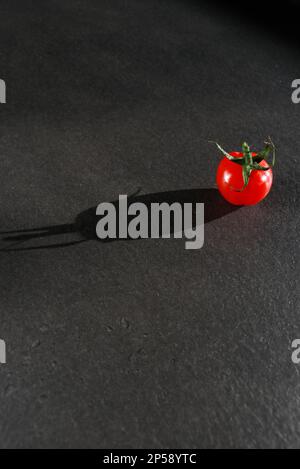 Eine Kirschtomate mit grünem Stiel, isoliert auf einem dunkelgrauen Marmortisch Stockfoto