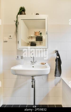 Ein Badezimmer mit Waschbecken, Spiegel und Handtuch, das an der Wand vor dem Waschbecken hängt, ist schwarz-weiß Stockfoto