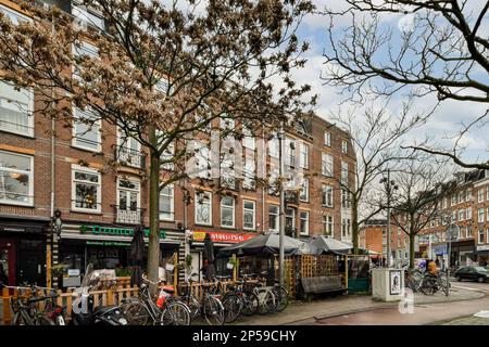 Amsterdam, Niederlande - 10. April 2021: Einige Fahrräder parken auf der Straßenseite vor einem Apartmentgebäude mit vielen Fenstern und Türen Stockfoto