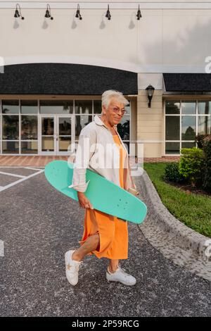 Ältere Frauen im orangefarbenen Kleid, die Skateboard halten Stockfoto