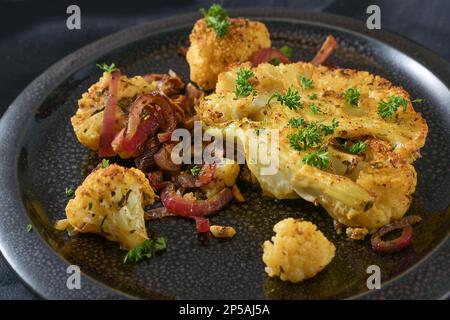 Gebackene, würzige Blumenkohlscheiben mit roten Zwiebeln auf einer schwarzen Platte, gesunde Gemüseschale für kohlenhydratarme Diät, Nahaufnahme, Kopierbereich, ausgewählter Fokus, Stockfoto