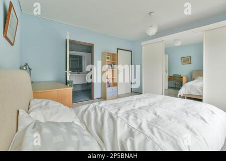 Ein Bett in einem Zimmer mit blauen Wänden und weißen Laken auf dem Bett, das über dem Kopfteil liegt Stockfoto