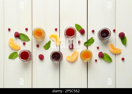 Gläser mit verschiedenen Marmeladen und frischen Zutaten auf weißem Holztisch, flach liegend Stockfoto