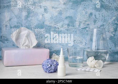 Nasentropfen mit Pillen, Blume, Glas Wasser und Taschentücher auf dem Tisch nahe der Grunge Wand. Saisonales Allergiekonzept Stockfoto