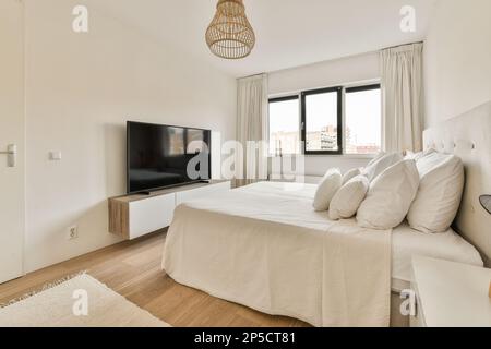 Ein Schlafzimmer mit einem großen Bett und einem fernseher an der Wand vor dem Bett ist an der Wand befestigt Stockfoto