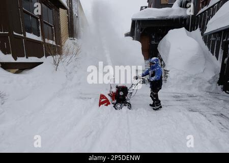 Ein Mann nutzt eine Schneeräummaschine, um eine Einfahrt zu räumen, während während während eines Schneesturms in Mammoth Lakes, CA, Schnee fällt. Stockfoto