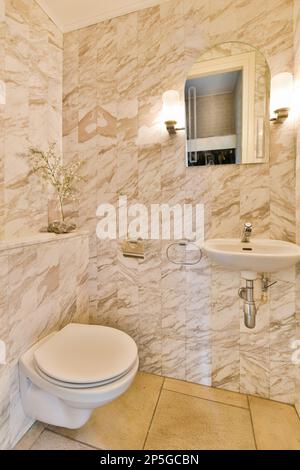 Ein kleines Badezimmer mit Marmorwänden und -Boden, inklusive einer weißen Toilette in der Ecke neben einem Waschbecken Stockfoto