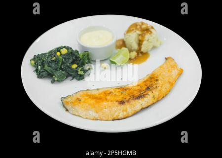 Gegrilltes Lachssteak mit Spinat und Sahne-Sauce auf schwarz isoliert. Stockfoto