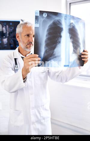 Er weiß genau, wonach er suchen muss. Ein reifer Arzt, der ein Röntgenbild untersucht. Stockfoto
