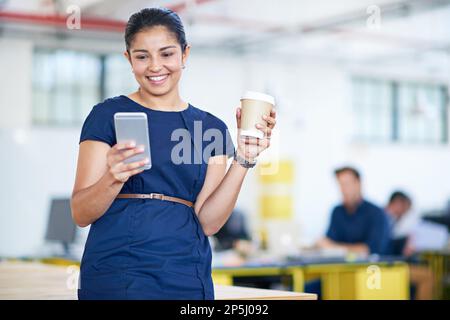 Ich habe ihre morgendlichen E-Mails durchgesehen. Eine attraktive junge Geschäftsfrau, die ein Handy in ihrem Büro benutzt. Stockfoto