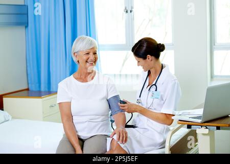 Es läuft gut unter Druck. Eine hübsche junge Ärztin, die den Blutdruck eines Seniorenpatienten testet. Stockfoto