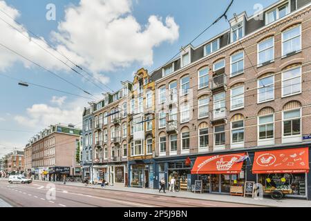 Eine Stadtstraße mit Gebäuden auf beiden Seiten und Geschäften in der Mitte der Straße stehen Autos entlang der Straße Stockfoto