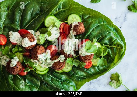 Falafel Wrap mit Gemüse und Tahini auf grünem Mangold, Draufsicht. Alternatives veganes Rezept. Stockfoto