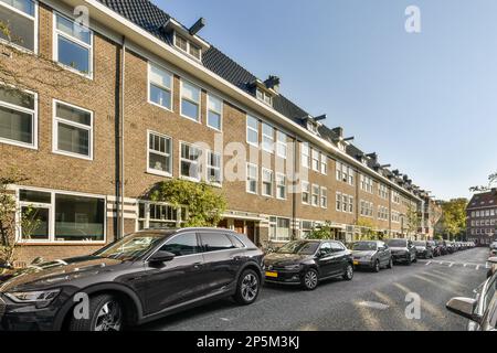 Autos parkten auf der Straße vor einem Ziegelgebäude mit vielen Fenstern und Rollläden zur Seite Stockfoto