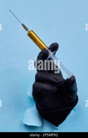 Handgehaltene Spritze mit gelbem Glitzer auf blauem Papierhintergrund. Vertikale Nahaufnahme. Stockfoto