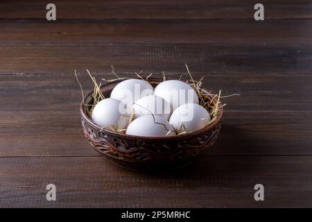 Weiße rohe Hühnereier liegen auf Heu in einer verbrannten Tonschüssel Stockfoto