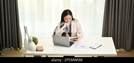 Blick über die asiatische Geschäftsführerin in elegantem Anzug, die mit einem Laptop an einem modernen Arbeitsplatz arbeitet Stockfoto