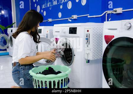 Das asiatische Mädchen wäscht Tücher in der Wäscherei an der Waschmaschine Stockfoto