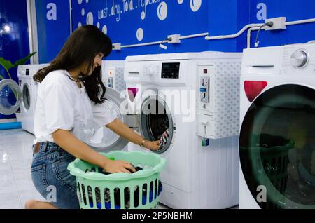 Das asiatische Mädchen wäscht Tücher in der Wäscherei an der Waschmaschine Stockfoto
