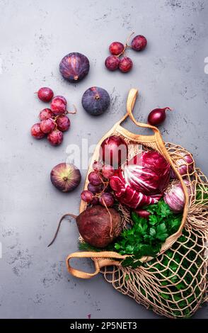 Hintergrund mit lila Gemüse, Wurzeln und Früchten in einer Einkaufstasche: Radicchio, Rote Bete, rote Zwiebeln, Trauben, Feigen. Ernte, lokaler Bauernhof Stockfoto